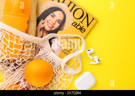 Schnur-Tasche mit frischen Orangen, Modemagazin und Strandaccessoires auf gelbem Hintergrund, flacher Lay. Leerzeichen für Text Stockfoto