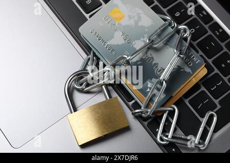 Cybersicherheit. Metallschloss mit Kette und Kreditkarten am Laptop, Draufsicht Stockfoto