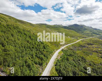 Drohnenfoto. Blick von oben auf ein norwegisches Bergtal mit einer Asphaltstraße in die Ferne unter einem blauen Himmel mit Cumuluswolken auf einem sonnigen s Stockfoto