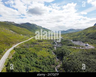 Drohnenfoto. Blick von oben auf ein norwegisches Bergtal mit einer Asphaltstraße in die Ferne unter einem blauen Himmel mit Cumuluswolken auf einem sonnigen s Stockfoto