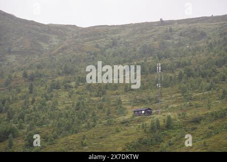 Norwegische Berglandschaft mit einem Holzhaus und einem Stromanschluss, an dem sich Internet- und Telefonantennen befinden. Stockfoto