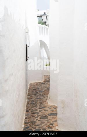 Ein malerischer Blick auf eine leere Straße in Binibeca, Menorca. Die weiß getünchten Gebäude und der kopfsteingepflasterte Pfad zeigen den bezaubernden mediterranen Bogen Stockfoto
