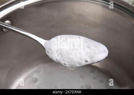 Chemische Reaktion von Essig und Backpulver in Löffel über Topf, Nahaufnahme Stockfoto