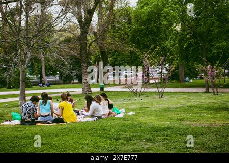 Madrid, Spanien. 1. Mai 2024 Eine Gruppe junger Menschen, die auf einem grünen Rasen im Sommerpark sitzen. Jugend auf einem Picknick im Park. Freunde im Freien. Kopierbereich. Stockfoto