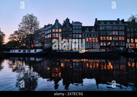 Niederlande, Amsterdam - 08. April 2024: Amsterdamer Grachtenhäuser, Fahrräder und Brücke im Stadtteil Jordaan bei Dämmerung Stockfoto