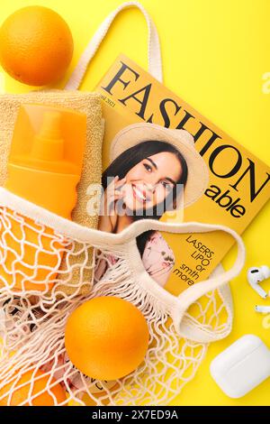 Schnur-Tasche mit frischen Orangen, Modemagazin und Strandaccessoires auf gelbem Hintergrund, flacher Lay Stockfoto