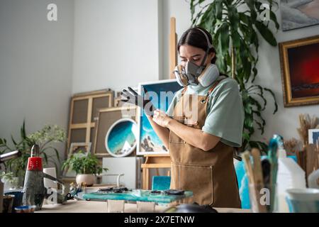 Nachdenkliche kreative Künstlerin im Atemschutzgerät, Latexhandschuhe, die sich auf die Arbeit mit Epoxidharz vorbereiten. Stockfoto