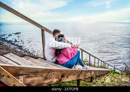 Ein junges verheiratetes Paar sitzt auf der langen Holztreppe und blickt auf das japanische Meer Stockfoto