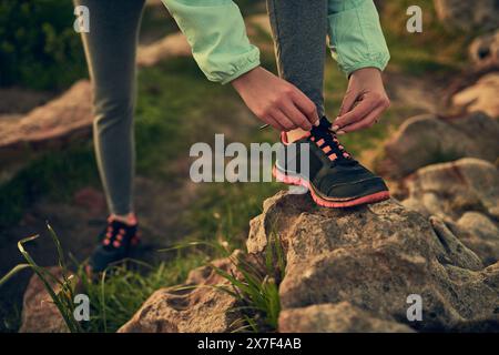 Person, Hände und Krawattenschuhe mit Felsen des Wanderers für einen Morgenspaziergang oder Trekking auf den Bergen im Freien. Nahaufnahme der Vorbereitung, Vorbereitung oder Bindung des Menschen Stockfoto