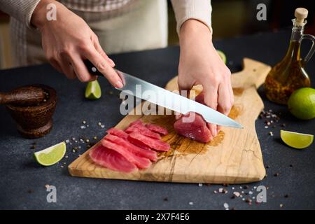 Frau Schnitt Thunfischsteak in Scheiben auf einem hölzernen Schneidebrett in der Hausküche Stockfoto