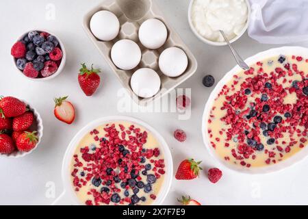 Kochen Herstellung von gebackenem Joghurt gesundes Dessert. Frau Hand kochen Ofen gebacken griechischer Joghurt Dessert mit frischen gefrorenen Beeren, auf weißem Küchentisch, mit Stockfoto