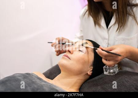 Pflanzenkosmetikerin, die Kosmetikgel mit Bürsten auf den Gesichtskunden im Schönheitssalon aufträgt Stockfoto