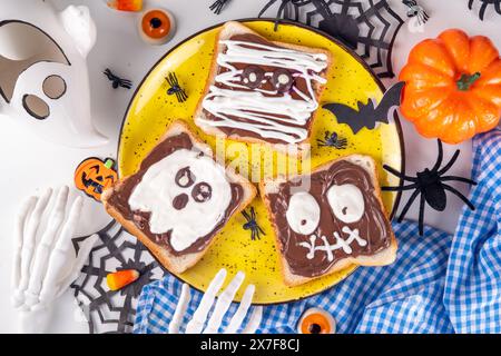 Lustige Halloween-Charaktere toasten Sandwiches mit Nüssen, Schokoladenbutter, Paste, Banane und geschmolzenem Marshmallow oder Joghurtnarben Dekor. Kreatives Halloween Stockfoto