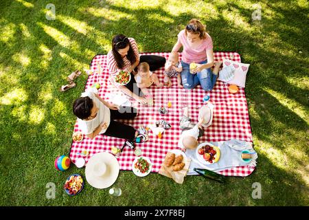 Mütter und Babys genießen ein Picknick im Freien im Park, sitzen auf einer Picknickdecke und bereiten Speisen und Getränke zu. Stockfoto