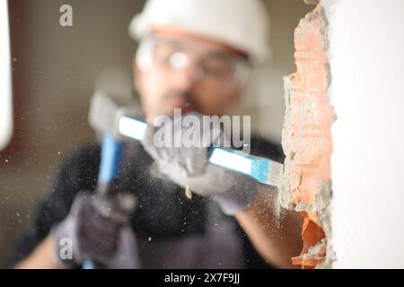 Bauarbeiter mit Steilhang und Hammer, um eine Mauer in einem Haus zu zerstören Stockfoto