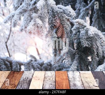 Weihnachtshintergrund. Leere Holztischplatte vor sonnigem Winterwald. Holzterrassenboden und Kiefernzweig mit Tannenzapfen bedeckt mit Fro Stockfoto