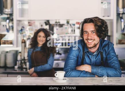Zwei junge Barista arbeiten im Café, stehen an der Theke. Universitätsstudenten arbeiten Teilzeit im Café. Stockfoto