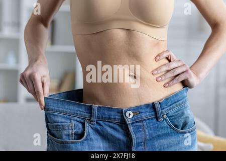 Nahaufnahme des weiblichen Körperteils, dünner Taillenbund, mit breiter Jeans und Ergebnis von Gewichtsverlust, Sport und Diät. Stockfoto