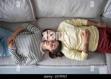 Glückliches junges Familienpaar, das sich nach dem Arbeitstag in einem hellen Wohnzimmerhaus auf dem Sofa entspannt. Stockfoto