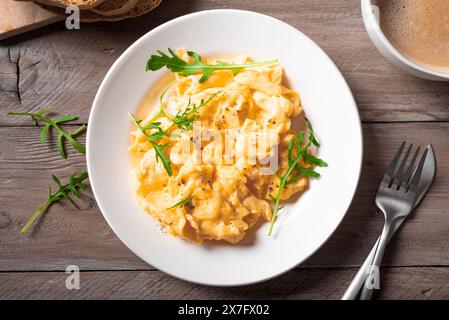 Rührei und eine Tasse Kaffee für ein gesundes Frühstück, Blick von oben. Flauschige Rührei auf weißem Teller. Stockfoto