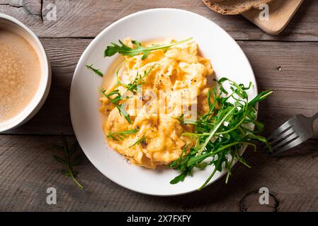 Rührei mit Rucola-Salat und einer Tasse Kaffee für ein gesundes Frühstück. Flauschige Rührei auf weißem Teller. Stockfoto