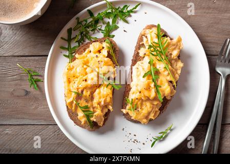 Rührei, Sandwiches und Kaffee für ein gesundes Keto-Frühstück. Vollkorntoast mit Rührei und Bio-Rucola-Mikrogrün auf weißer Platte, Stockfoto