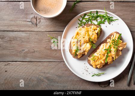 Rührei, Sandwiches und Kaffee für ein gesundes Keto-Frühstück. Vollkorntoast mit Rührei und Bio-Rucola-Mikrogrün auf Holztisch Stockfoto