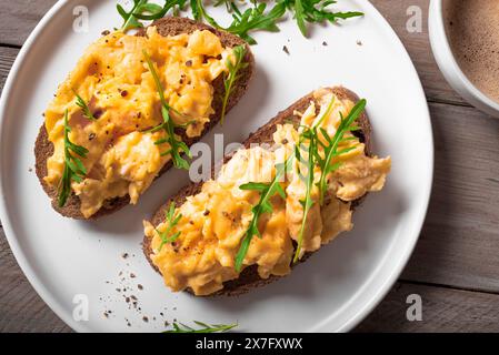 Rührei-Sandwiches für ein gesundes Keto-Frühstück. Vollkorntoast mit Rührei und Bio-Rucola-Mikrogrün auf weißer Platte in Nahaufnahme. Stockfoto