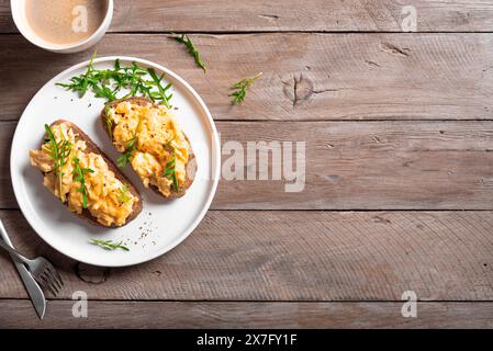 Rührei, Sandwiches und Kaffee für ein gesundes Keto-Frühstück. Vollkorntoast mit Rührei und Bio-Rucola-Mikrogrün auf Holztisch Stockfoto