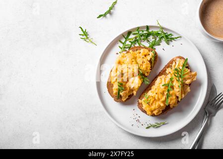 Rührei, Sandwiches und Kaffee für ein gesundes Keto-Frühstück. Vollkorntoast mit Rührei und Bio-Rucola-Mikrogrün auf weißem Tisch, Stockfoto