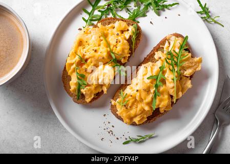 Rührei, Sandwiches und Kaffee für ein gesundes Keto-Frühstück. Vollkorntoast mit Rührei und Bio-Rucola-Mikrogrün auf weißem Tisch, Stockfoto