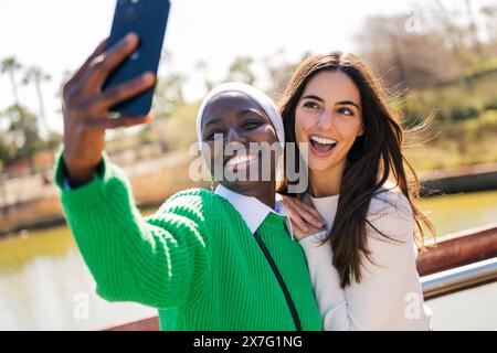 Zwei junge Freundinnen lächeln glücklich, während sie Spaß haben, Selfie-Fotos mit Handy in einem Stadtpark zu machen, Konzept der Freundschaft und moderner Lebensstil Stockfoto