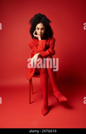 Eine junge Frau in einem auffälligen roten Kleid, die anmutig auf einem leuchtend roten Stuhl sitzt. Stockfoto