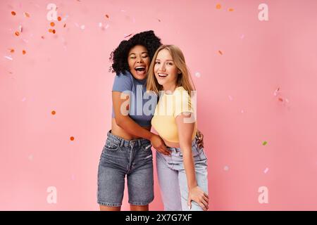 Zwei attraktive junge Frauen in kuscheliger Kleidung stehen nebeneinander vor einem leuchtend rosa Hintergrund. Stockfoto