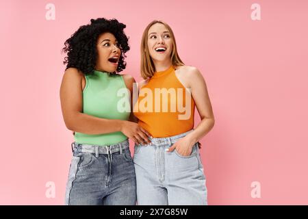 Zwei schöne, vielfältige Frauen in kuscheliger Freizeitkleidung stehen nebeneinander vor einem rosa Hintergrund. Stockfoto