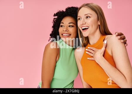 Zwei stilvolle Damen in legeren Kleidern stehen elegant vor einem leuchtend rosa Hintergrund. Stockfoto