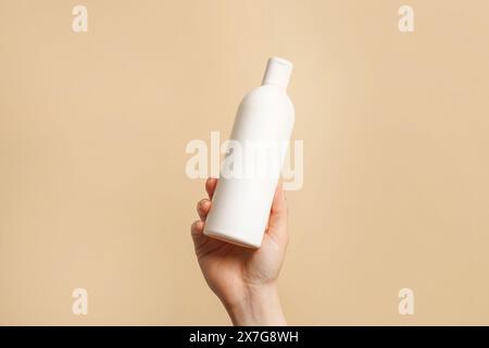 Hand hält weiße Flasche Shampoo oder Haarspülung auf beigefarbenem Hintergrund, Kopierraum Stockfoto