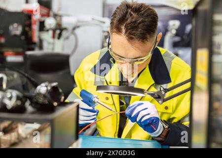 Elektriker Techniker kaukasischer Mann mit heißem Lötkolben, um Elektrizitätsdraht zu verbinden, reparieren Sie Stromkabel mit Lötzinn und lea Stockfoto