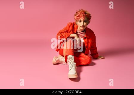 Eine Frau in lebendiger Kleidung sitzt friedlich auf dem Boden vor rosa Hintergrund. Stockfoto
