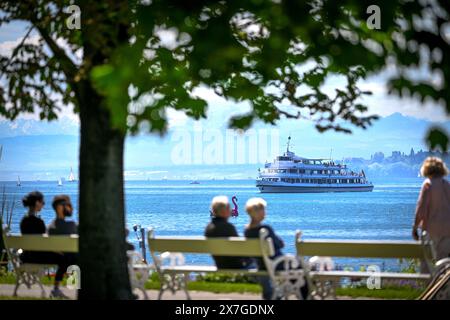 20. Mai 2024, Baden-Württemberg, Überlingen am Bodensee: Das Fahrgastschiff Stuttgart fährt auf dem Bodensee bis zur Anlegestelle, während im Vordergrund zwei Paare auf den Bänken im Seepark sitzen. Foto: Felix Kästle/dpa Stockfoto