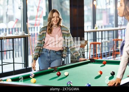 Zwei Frauen, Kollegen in einem Coworking-Bereich, spielen ein freundliches Billard-Spiel und präsentieren Teamwork und modernen Geschäftsstil. Stockfoto