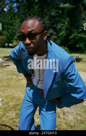 Hübscher afroamerikanischer Mann mit elegantem Stil posiert in einem lebhaften grünen Garten. Stockfoto