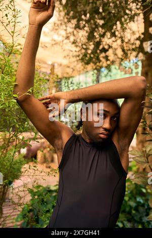 Raffinierter afroamerikanischer Mann mit elegantem Stil, der im grünen Garten die Arme hebt. Stockfoto