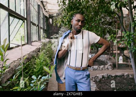 Hübscher afroamerikanischer Mann in elegantem Stil, mit weißem Hemd und blauer Hose, posiert in einem lebhaften grünen Garten. Stockfoto