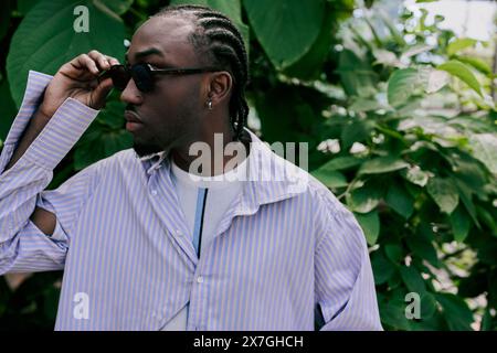 Ein raffinierter, gutaussehender Afroamerikaner mit Dreadlocks, der anmutig vor einem lebhaften grünen Busch steht. Stockfoto