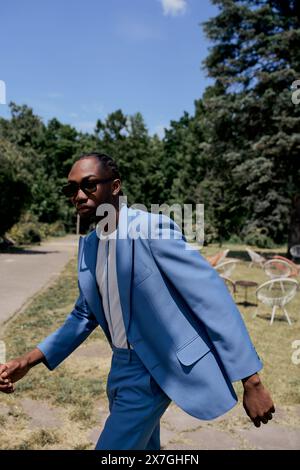 Stilvoller afroamerikanischer Mann in blauem Anzug geht selbstbewusst auf dem Bürgersteig entlang. Stockfoto