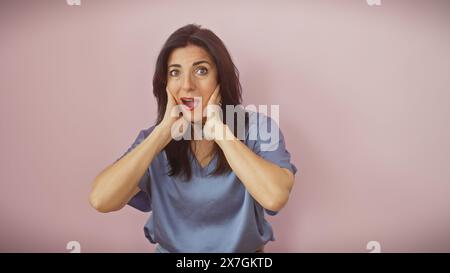 Überraschte hispanische Frau mittleren Alters mit breiten Augen und offenem Mund, vor einem rosa Hintergrund stehend. Stockfoto