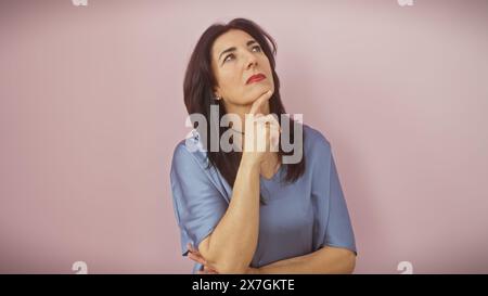 Nachdenkliche hispanische Frau in Besinnung, isoliert auf einem rosa Hintergrund, die Reife und Eleganz darstellt. Stockfoto