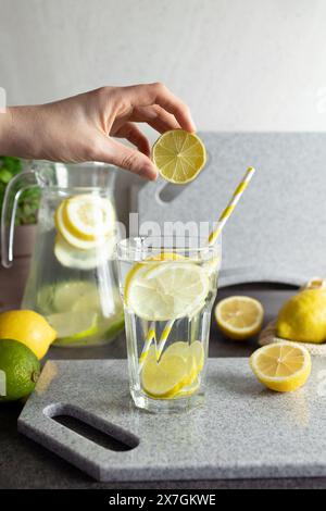 Frau Hand hält Zitronenscheibe über Glas Limonade Stockfoto