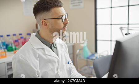 Schöner junger Mann mit Bart, Labormantel und Brille, der am Computer im Labor arbeitet Stockfoto